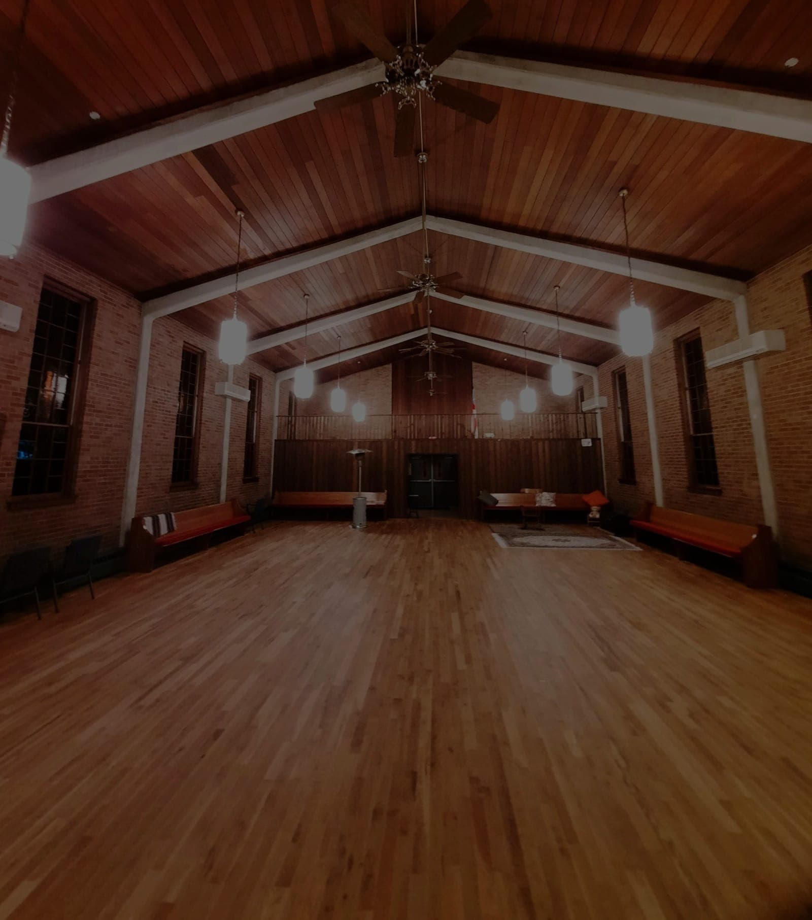 An empty dance hall with a peaked wooden ceiling and hardwood floor, before the dance